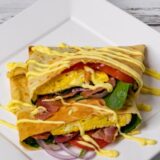 Crepe with bacon, eggs, spinach, and tomatoes, topped with Hollandaise sauce, on an elegant white plates