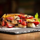Strawberry and banana crepe with chocolate drizzle on table and black slate stone