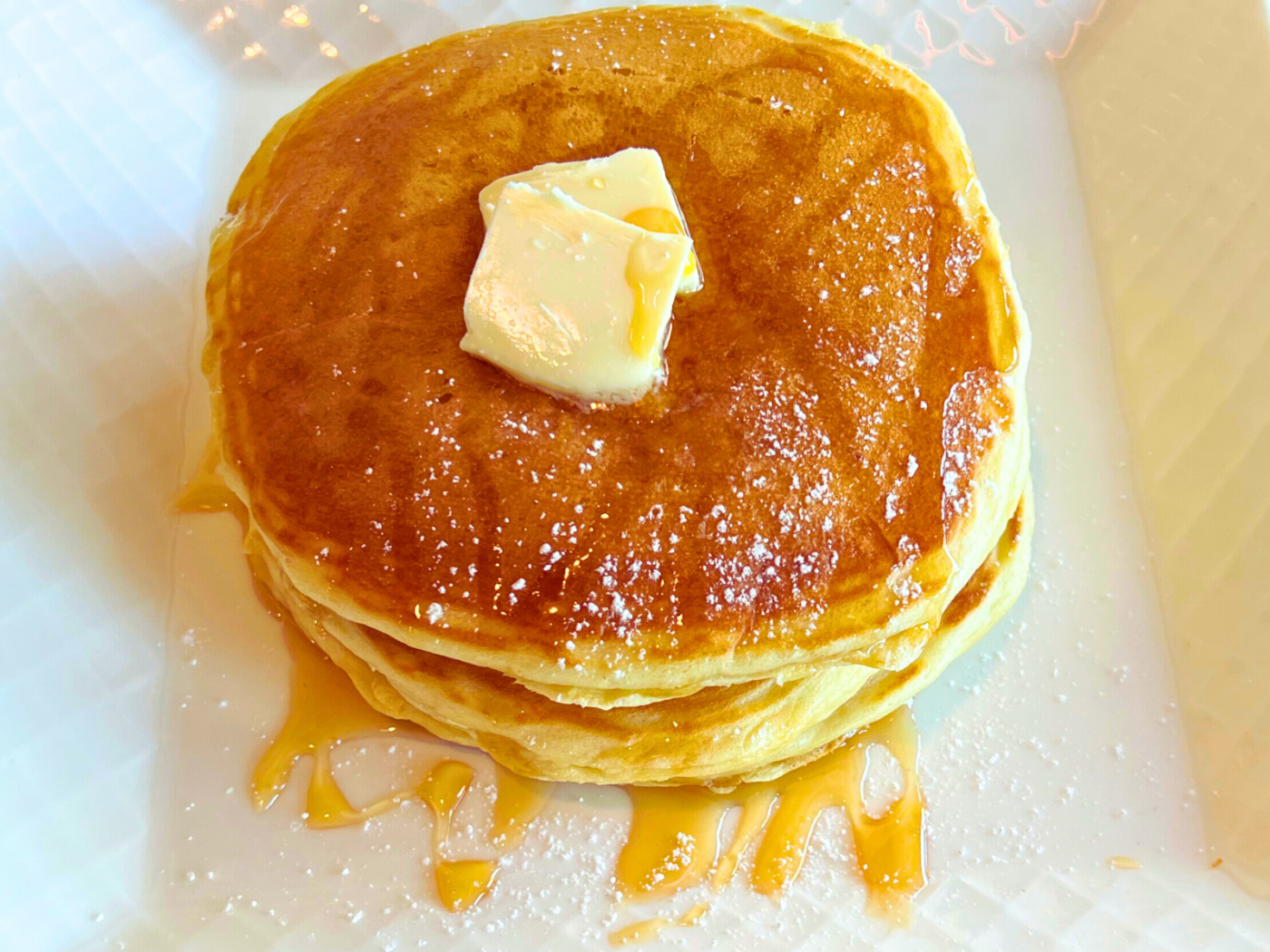 Stack of three pancakes with butter and maple syrup on top served on a plate