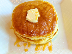 Stack of three pancakes with butter and maple syrup on top served on a plate