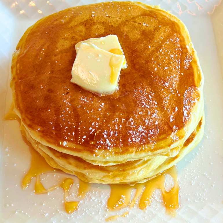 Stack of three pancakes with butter and maple syrup on top served on a plate