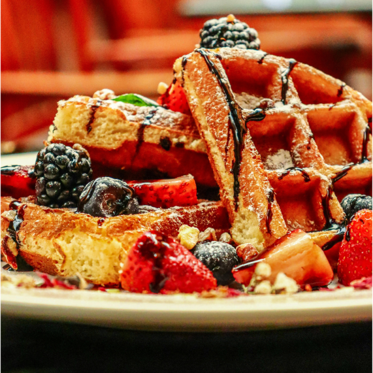 Belgian Waffle cut to quarter, fruits added on top with syrup and chocolates.